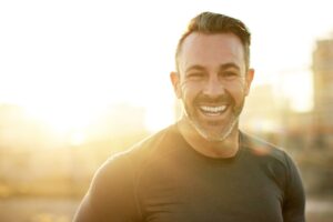 Laugh, fitness and man in city in morning for exercise, marathon training and cardio workout. Sports, sunshine and happy person for rest, recovery and health for performance, endurance and running